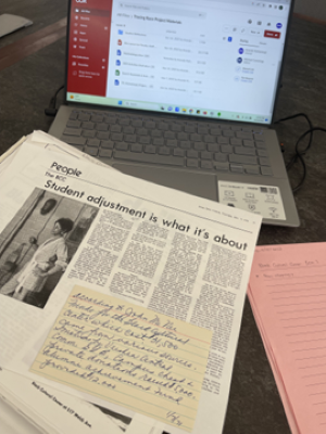 An open laptop with a photocopied newspaper article and hand-written note