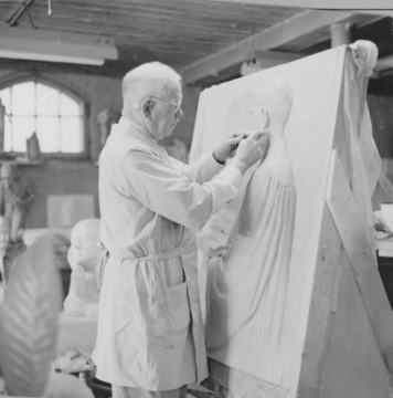 Older white man with with white hair, glasses, and lab coat sketching a person on a large white surface