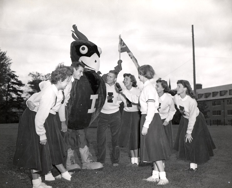 Big red bird mascot with capital I on chest surrounded by 2 male and 6 femail cheerleaders.