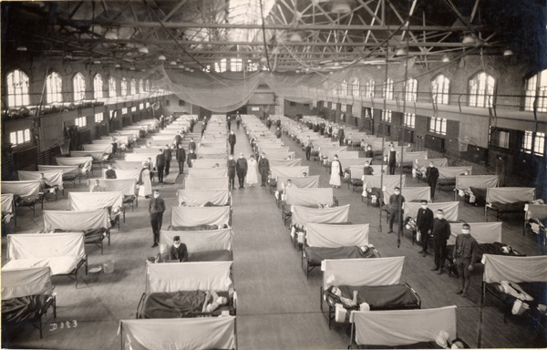 Over 100 beds with sheets in between them seen from above in a large gymnasium