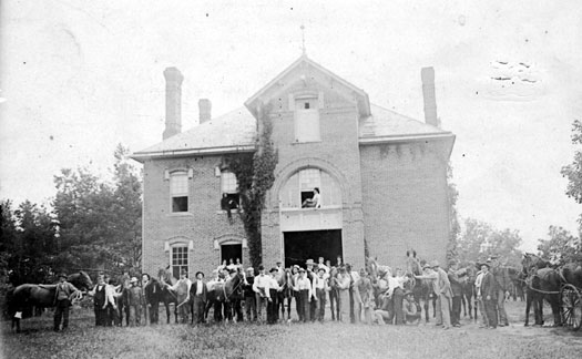Many people standing in a line with two horses in front of a large two story building