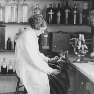Black and whit image of woman scientist sitting at lab 