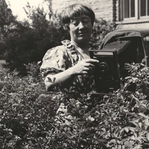 Black and white image of Ada Hayden in a bush taking a photo of the plant