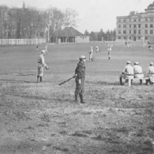 Black and white image of baseball athletes playing the game with Beardshear far in the back