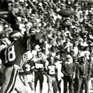 Black and white image of football player throwing a football in front of full stadium behind c. 1970's    